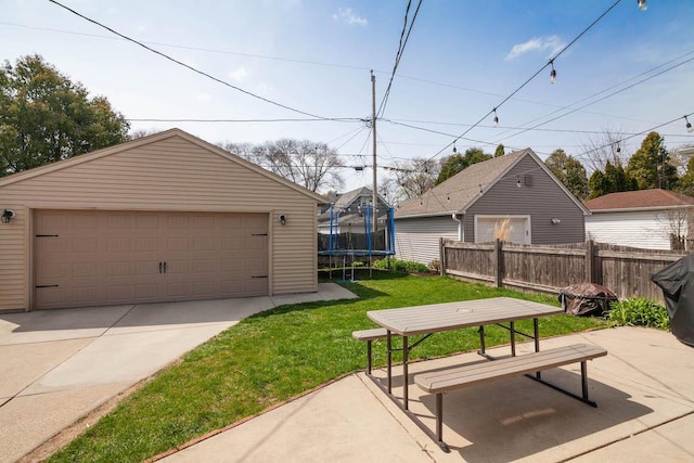 view of yard featuring an outdoor structure, a garage, a trampoline, and fence