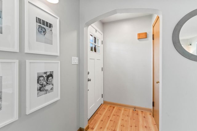 doorway with arched walkways, baseboards, and light wood finished floors
