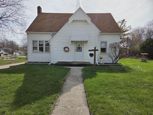 view of front of house with a shingled roof, board and batten siding, a front yard, and a chimney