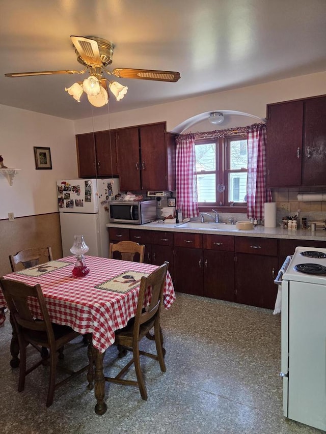 kitchen with dark brown cabinetry, a sink, white appliances, arched walkways, and light countertops