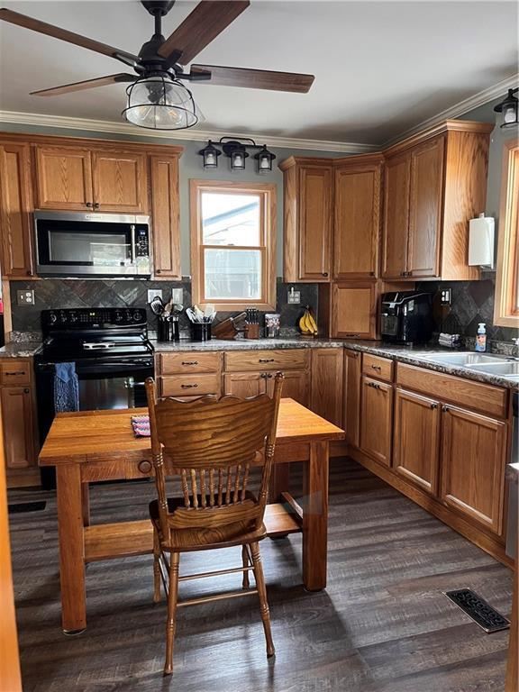 kitchen featuring black range with electric stovetop, stainless steel microwave, and brown cabinets