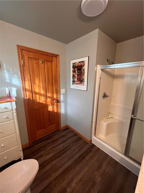 bathroom featuring toilet, baseboards, wood finished floors, and a shower stall