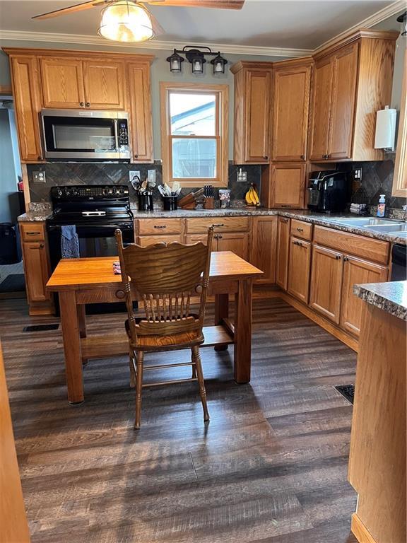 kitchen with stainless steel microwave, brown cabinetry, crown molding, backsplash, and electric range