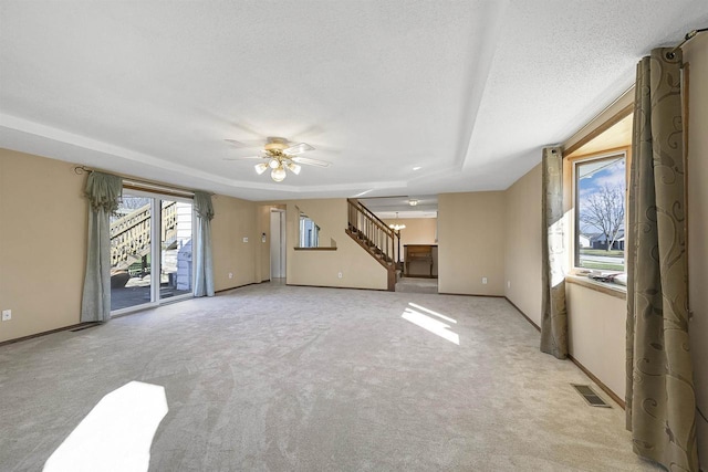 1992 London Rd, Green Bay, WI 54311 - unfurnished living room with a ceiling fan, light colored carpet, visible vents, a tray ceiling, and stairs