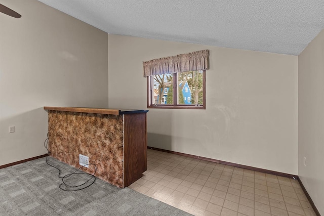 bar featuring a ceiling fan, a textured ceiling, vaulted ceiling, baseboards, and a bar