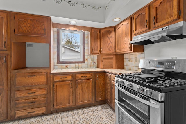kitchen with brown cabinetry, double oven range, tasteful backsplash, tile counters, and under cabinet range hood