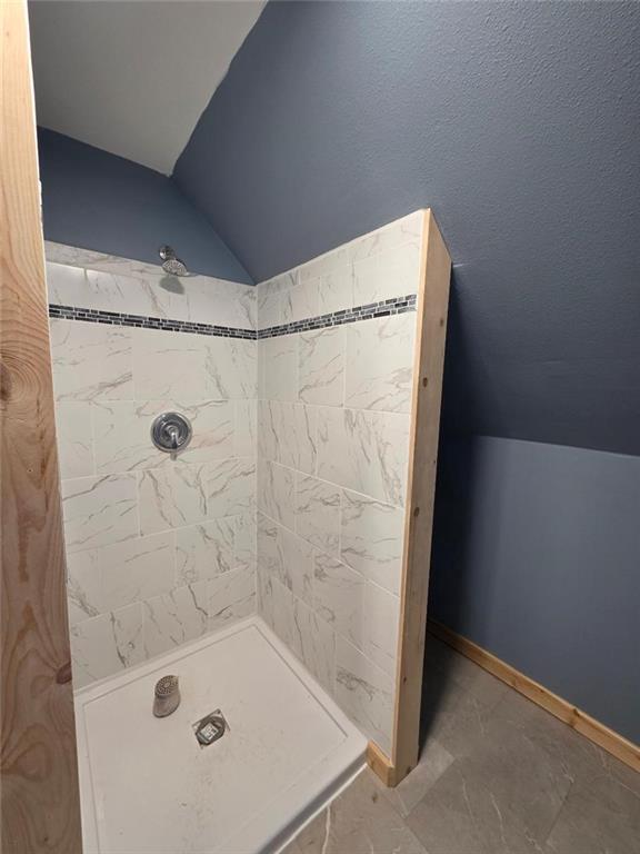 bathroom with baseboards, a shower stall, and vaulted ceiling