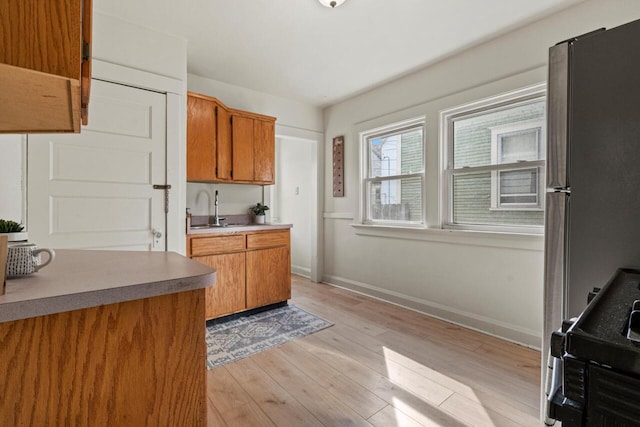 817 E Otjen St, Milwaukee, WI 53207 - kitchen with a sink, brown cabinetry, light wood-style flooring, freestanding refrigerator, and baseboards