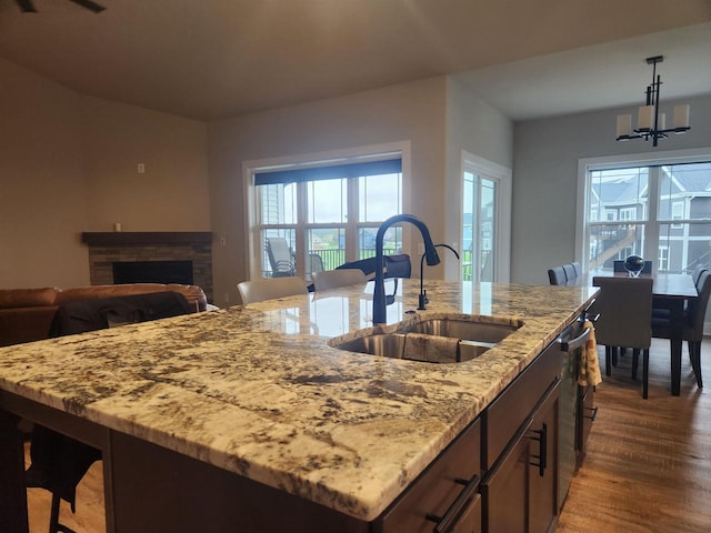 kitchen with a sink, a fireplace, a center island with sink, decorative light fixtures, and dark wood-style floors