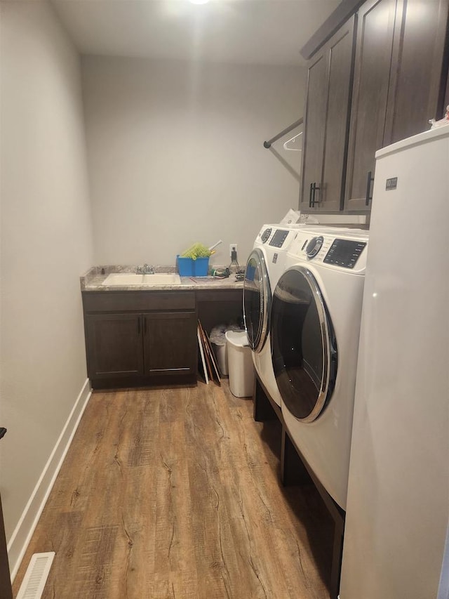 washroom featuring cabinet space, a sink, baseboards, light wood-type flooring, and washer and clothes dryer