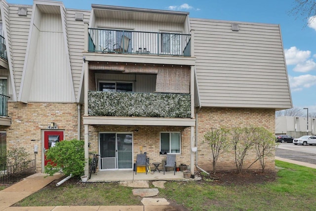 rear view of house featuring brick siding, a patio area, and a balcony