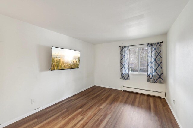 unfurnished room featuring baseboards, a baseboard heating unit, and wood finished floors