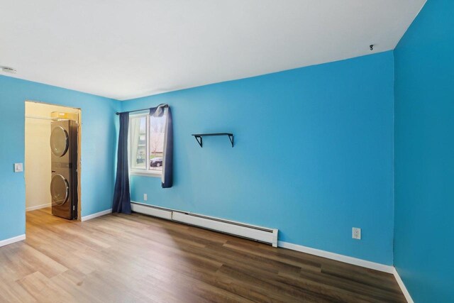 unfurnished bedroom featuring baseboards, a baseboard radiator, stacked washer and clothes dryer, and wood finished floors