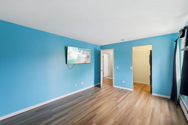 unfurnished bedroom with baseboard heating, baseboards, and wood finished floors
