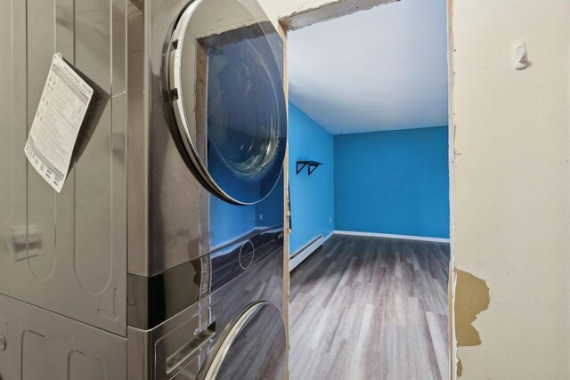 laundry area featuring laundry area, stacked washer / drying machine, wood finished floors, baseboards, and a baseboard radiator
