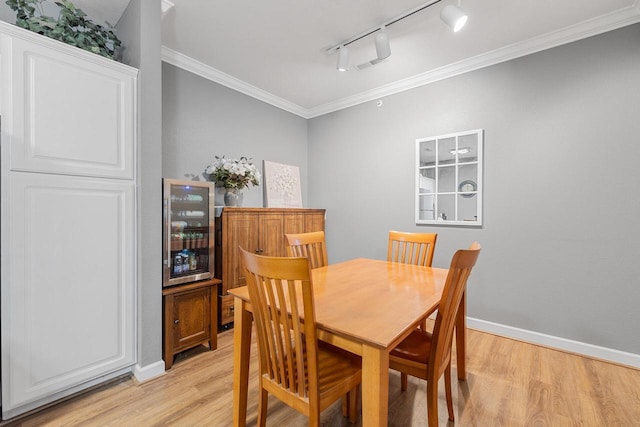 dining area with beverage cooler, rail lighting, light wood-style flooring, and ornamental molding