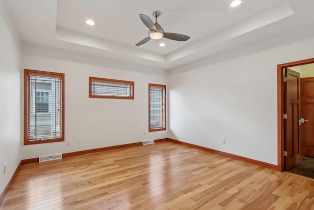 spare room with visible vents, a ceiling fan, a raised ceiling, and light wood-type flooring