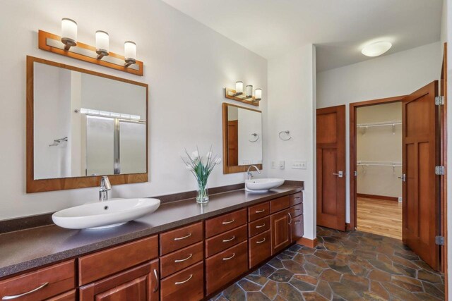 bathroom featuring a sink, a walk in closet, stone finish flooring, and double vanity