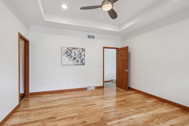 spare room with ceiling fan, visible vents, a raised ceiling, and light wood-style floors