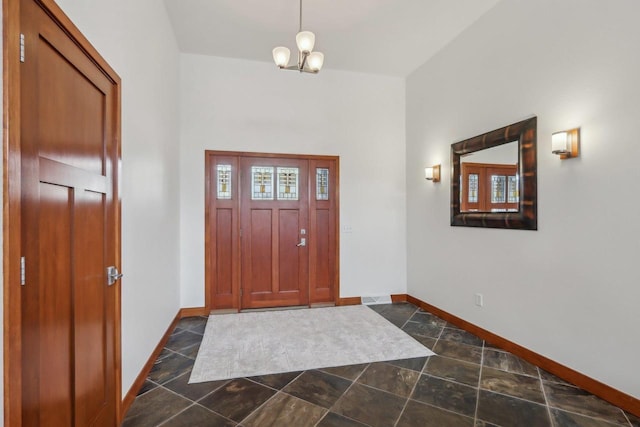 foyer entrance with baseboards, an inviting chandelier, and stone finish floor