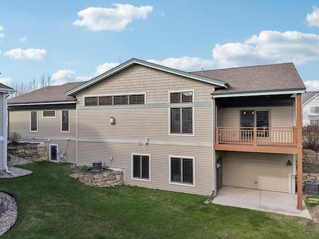 rear view of house with a lawn, central AC unit, a balcony, a patio, and a shingled roof