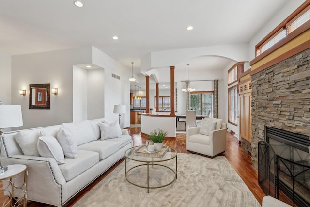 living area featuring arched walkways, a stone fireplace, recessed lighting, wood finished floors, and visible vents