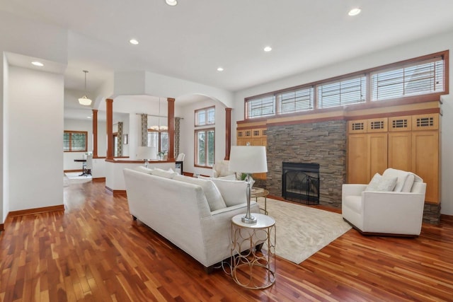living room with wood finished floors, baseboards, a stone fireplace, recessed lighting, and arched walkways
