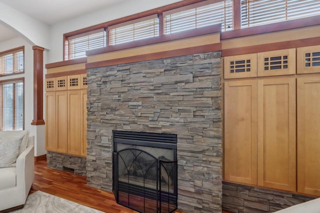 unfurnished living room with arched walkways, ornate columns, a stone fireplace, and wood finished floors