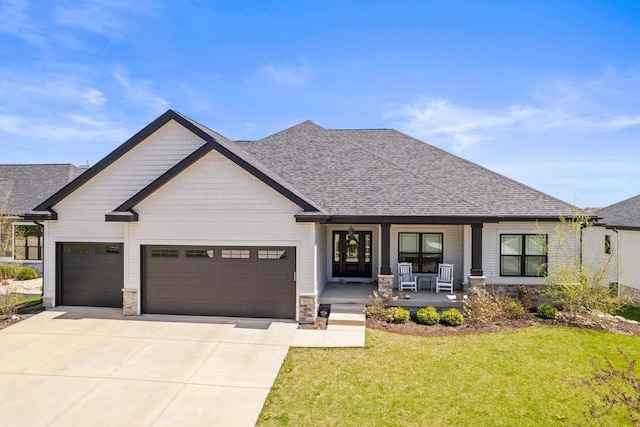 view of front of house with an attached garage, stone siding, a front yard, a porch, and driveway
