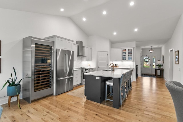 kitchen with a kitchen island with sink, appliances with stainless steel finishes, a sink, wine cooler, and wall chimney exhaust hood