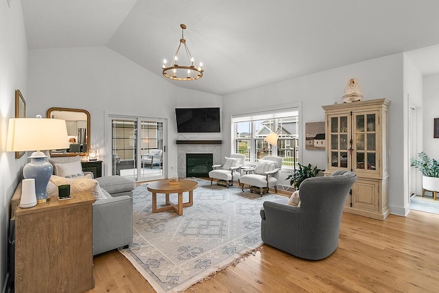 living room featuring an inviting chandelier, light wood finished floors, a fireplace, and high vaulted ceiling