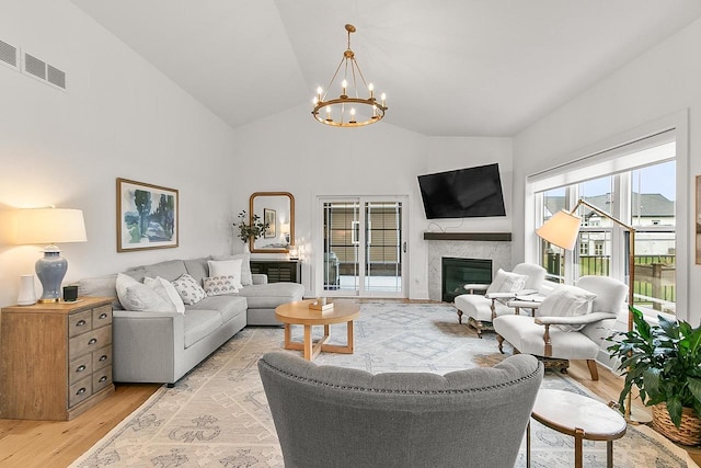 living area with a fireplace, high vaulted ceiling, a chandelier, light wood-type flooring, and visible vents