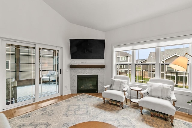 living room featuring a high end fireplace, vaulted ceiling, wood finished floors, and visible vents