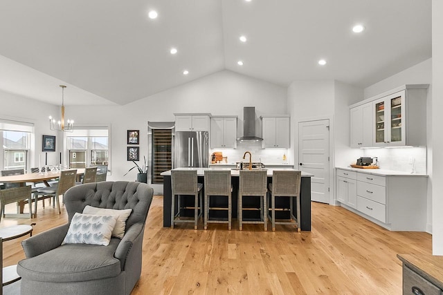 kitchen featuring light countertops, freestanding refrigerator, an inviting chandelier, a breakfast bar, and wall chimney exhaust hood