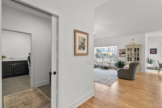 corridor featuring washer / dryer, baseboards, light wood-style floors, and a sink