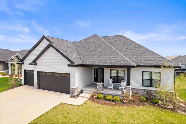 view of front of house with a porch, a front lawn, stone siding, and a garage
