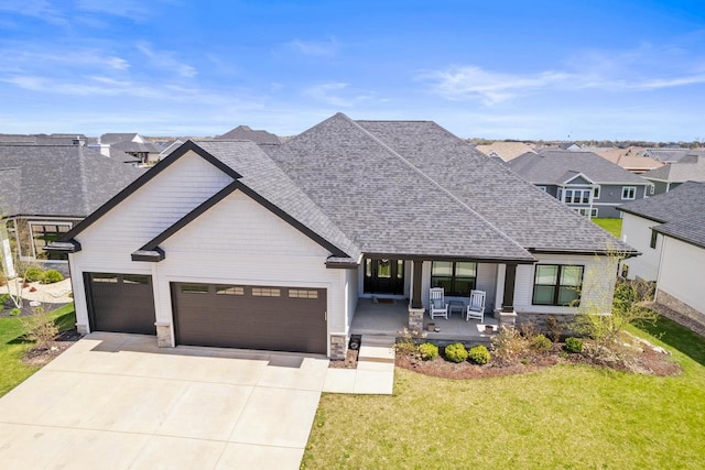 view of front of home featuring an attached garage, stone siding, a front yard, concrete driveway, and a porch