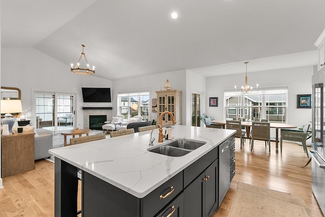 kitchen with a sink, light wood-style flooring, a glass covered fireplace, and a notable chandelier