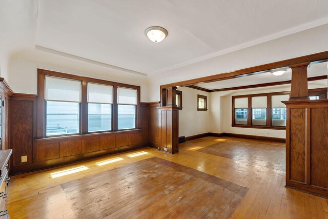 unfurnished living room featuring light wood-style floors, crown molding, and ornate columns