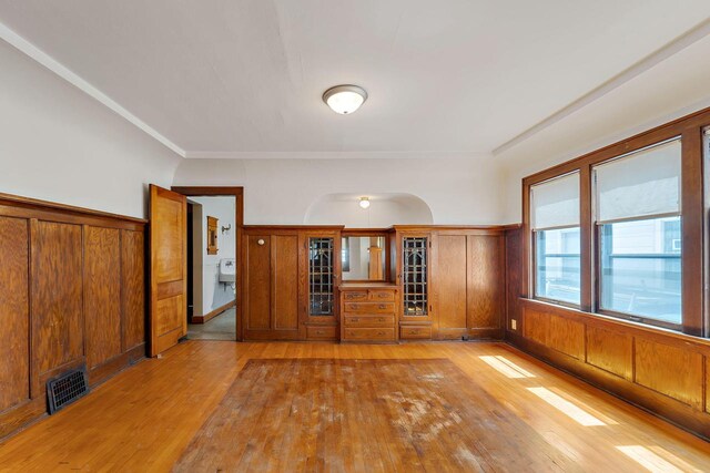 spare room featuring visible vents, light wood finished floors, crown molding, and a wainscoted wall