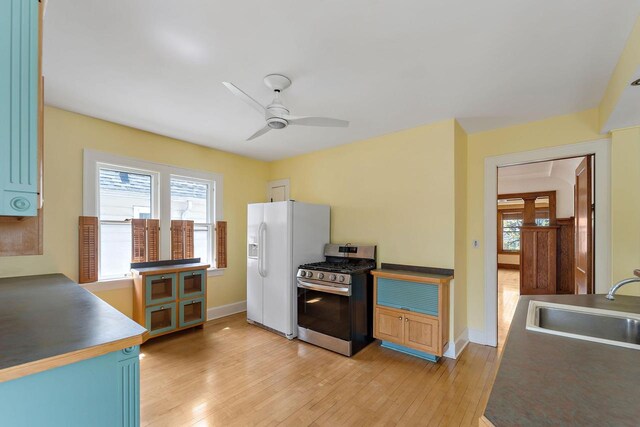 kitchen with ceiling fan, a sink, white refrigerator with ice dispenser, light wood-style flooring, and stainless steel range with gas cooktop