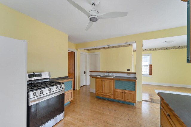 kitchen featuring a sink, light wood-style floors, stainless steel range with gas cooktop, freestanding refrigerator, and baseboards