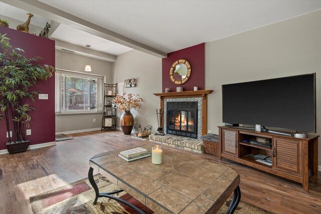 living area with beamed ceiling, baseboards, wood finished floors, and a tile fireplace