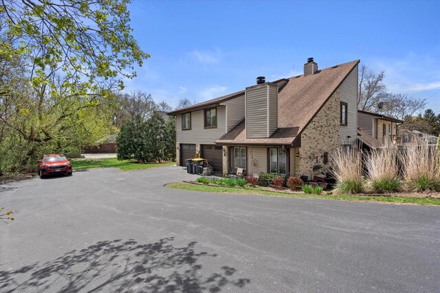 view of front of home with a garage, a chimney, a shingled roof, and aphalt driveway