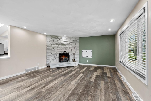 unfurnished living room featuring visible vents, a stone fireplace, and wood finished floors