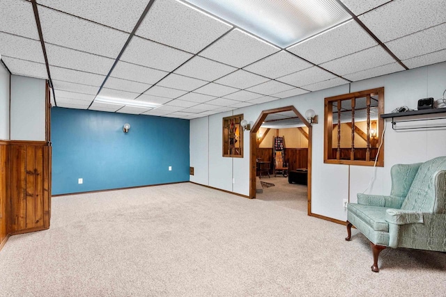 finished below grade area featuring carpet flooring, baseboards, wood walls, and a drop ceiling