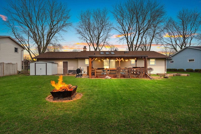 back of house featuring a storage unit, an outdoor fire pit, a patio, an outdoor structure, and a yard