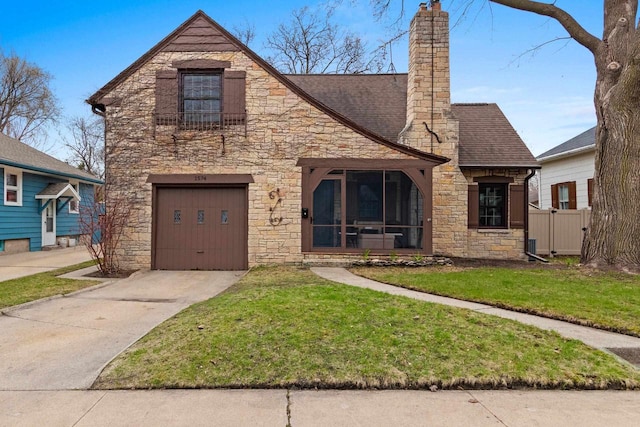 tudor house featuring an attached garage, a front lawn, stone siding, a chimney, and driveway