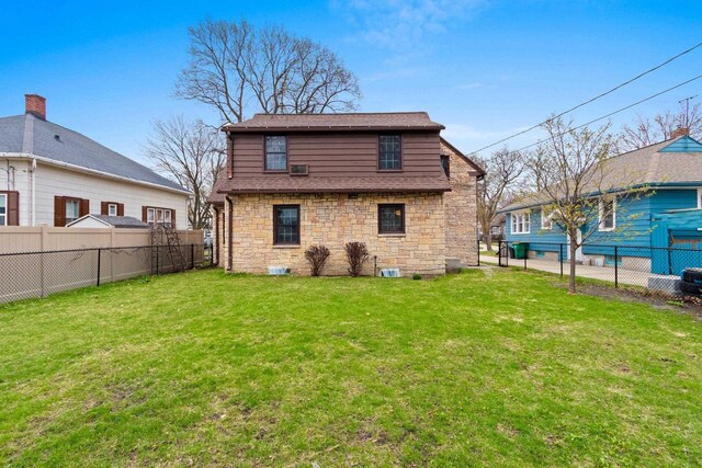 rear view of house with a yard, a fenced backyard, and stone siding