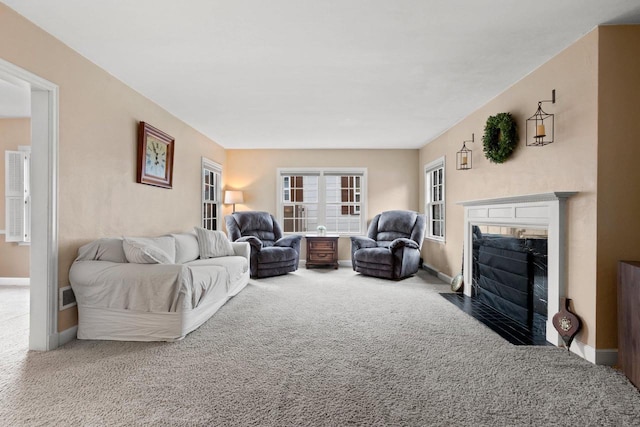 living area featuring baseboards, a fireplace with flush hearth, and carpet